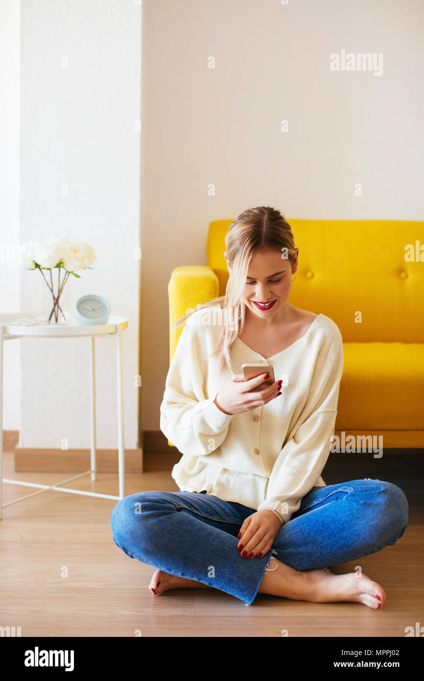 Blonde woman using smartphone à la maison Banque D'Images