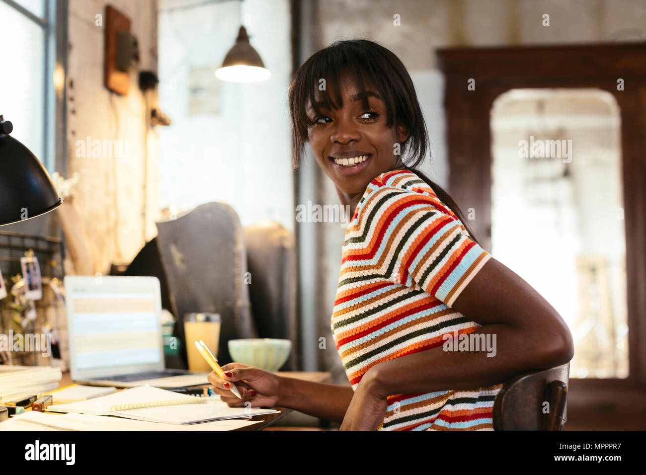Portrait of smiling young woman sitting at desk dans un loft Banque D'Images