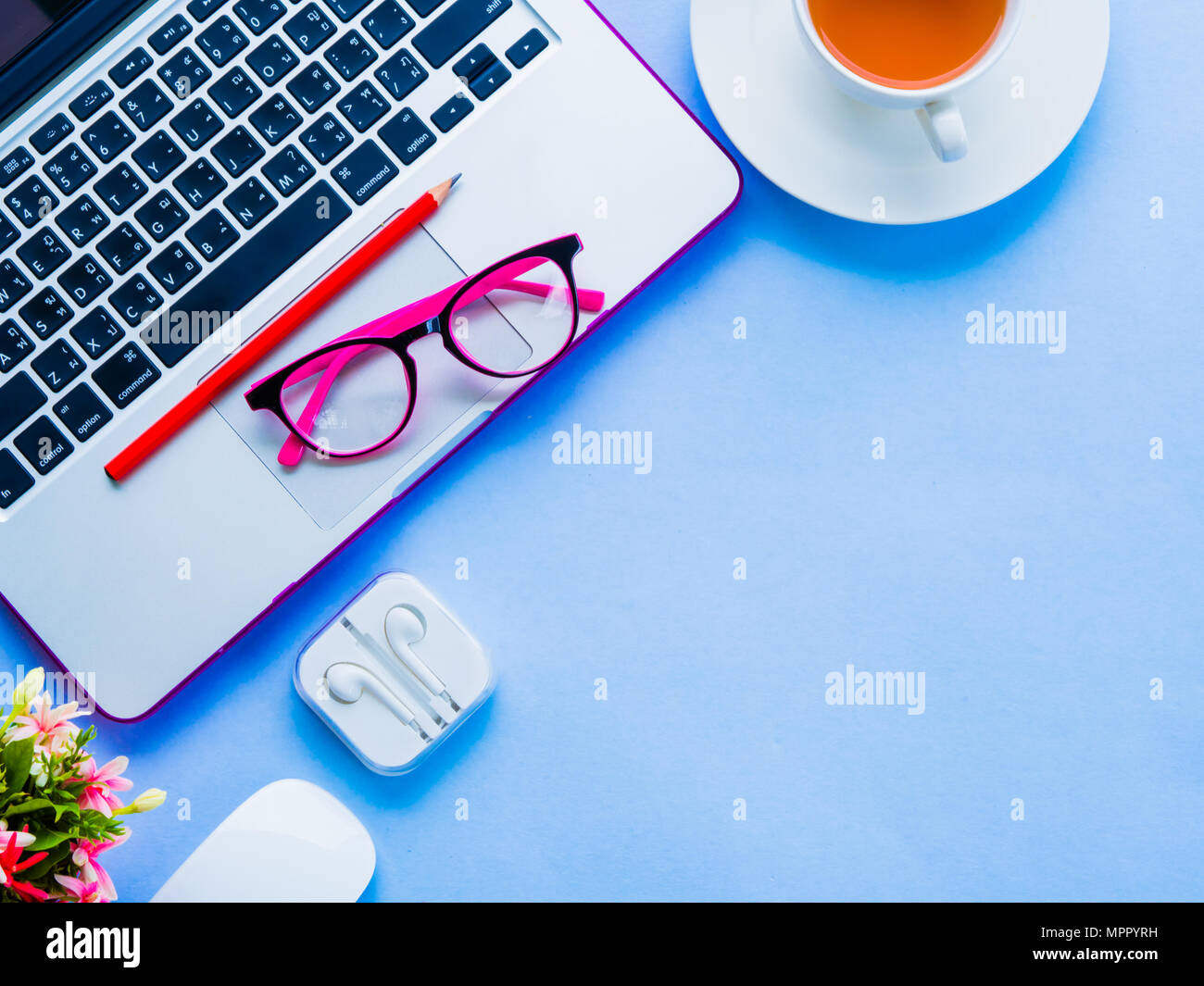Espace de bureau féminin avec accessoires de bureau avec ordinateur portable, café, crayon rouge, fleurs, souris et lunettes roses sur fond bleu. Banque D'Images