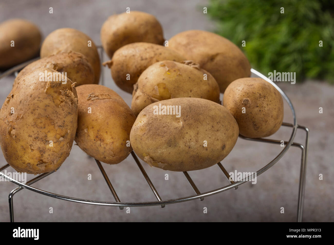 Groupe de nouvelles pommes de terre sur une grille métallique avec quelques herbes vertes en arrière-plan Banque D'Images