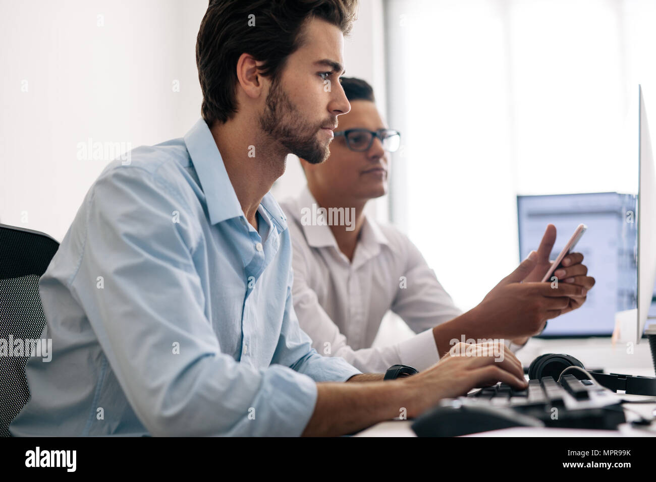 Les développeurs d'application de test sur téléphone mobile au bureau. Les développeurs de logiciels de bureau à travailler sur des ordinateurs. Banque D'Images
