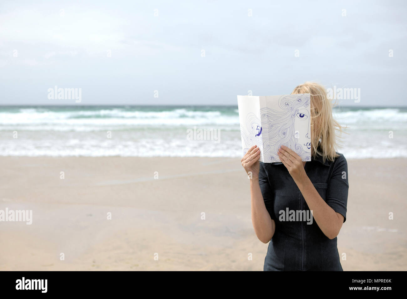 Woman covering face au livre, la lecture de poèmes sur la plage Banque D'Images