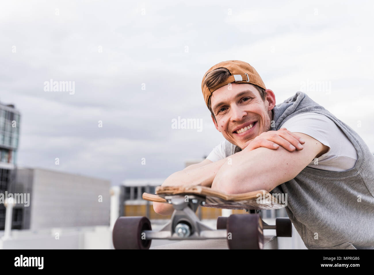 Portrait of smiling man with skateboard appuyée sur un mur Banque D'Images
