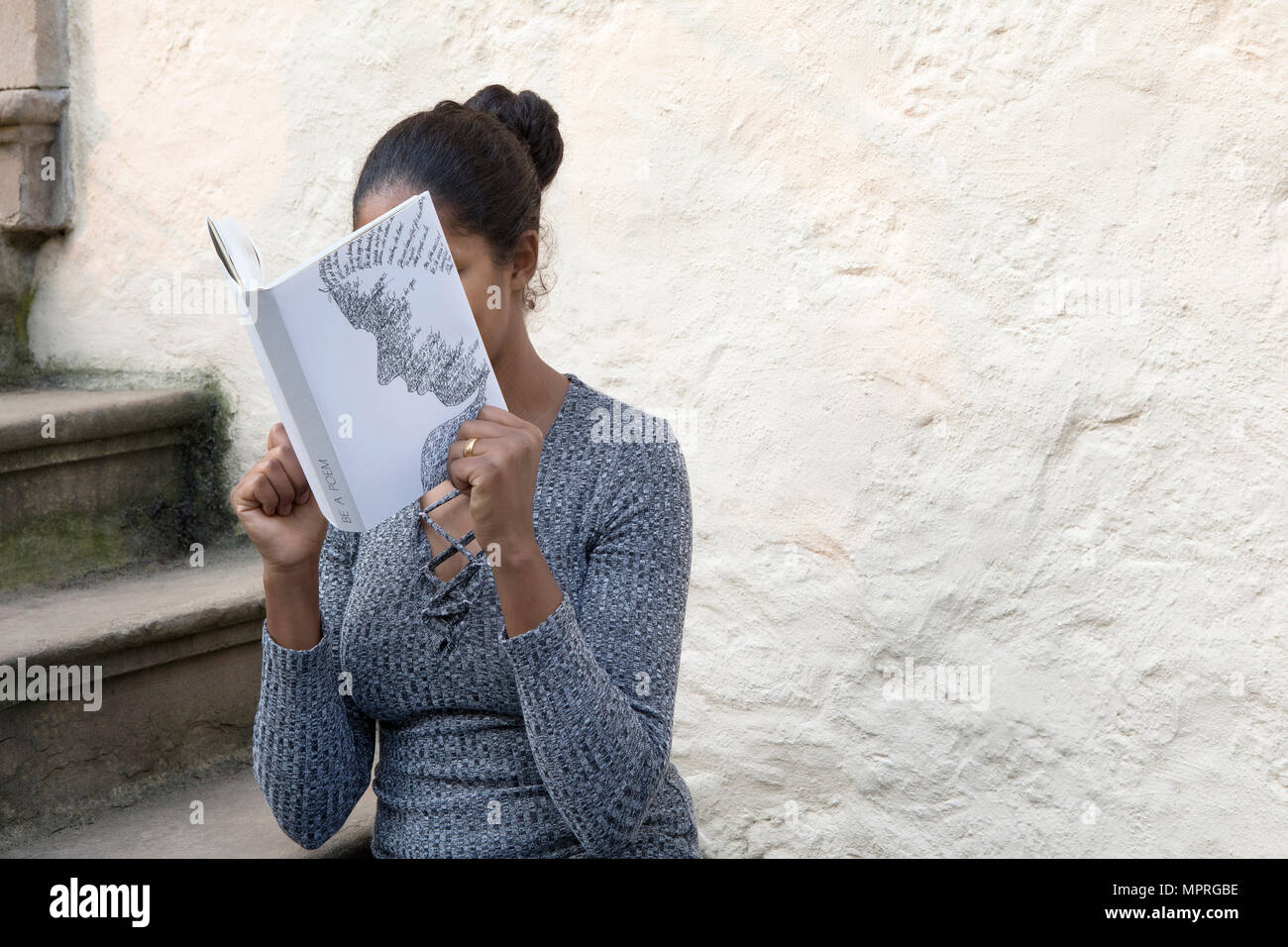 Woman covering face au livre, la lecture de poèmes en face de wall Banque D'Images