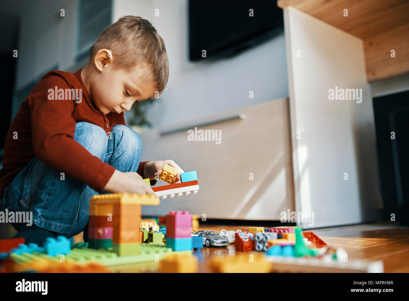 Petit garçon accroupi sur le plancher à la maison à jouer avec des briques de bâtiment Banque D'Images