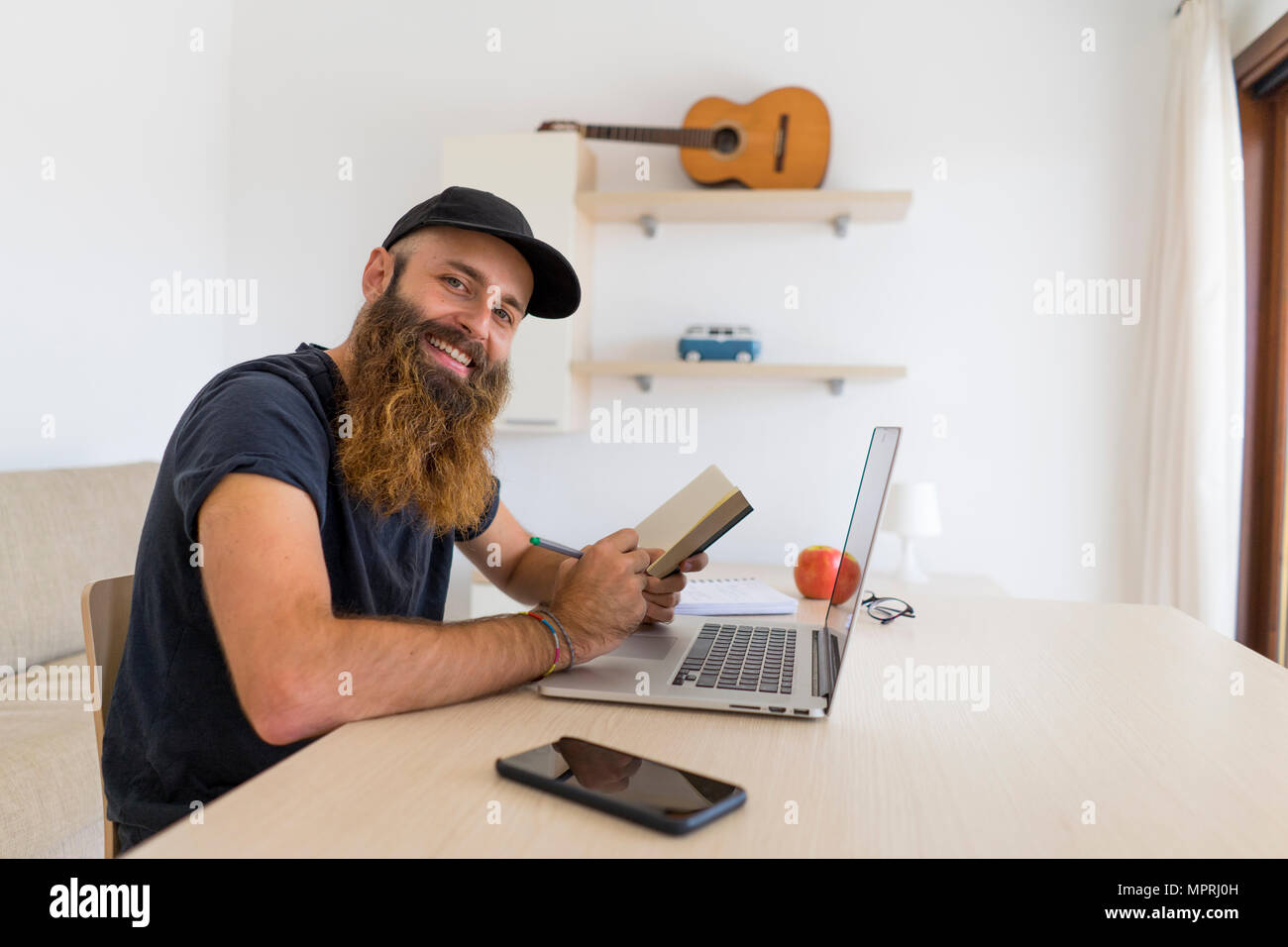 Portrait de jeune homme barbu assis à un bureau avec ordinateur portable et ordinateur portable Banque D'Images
