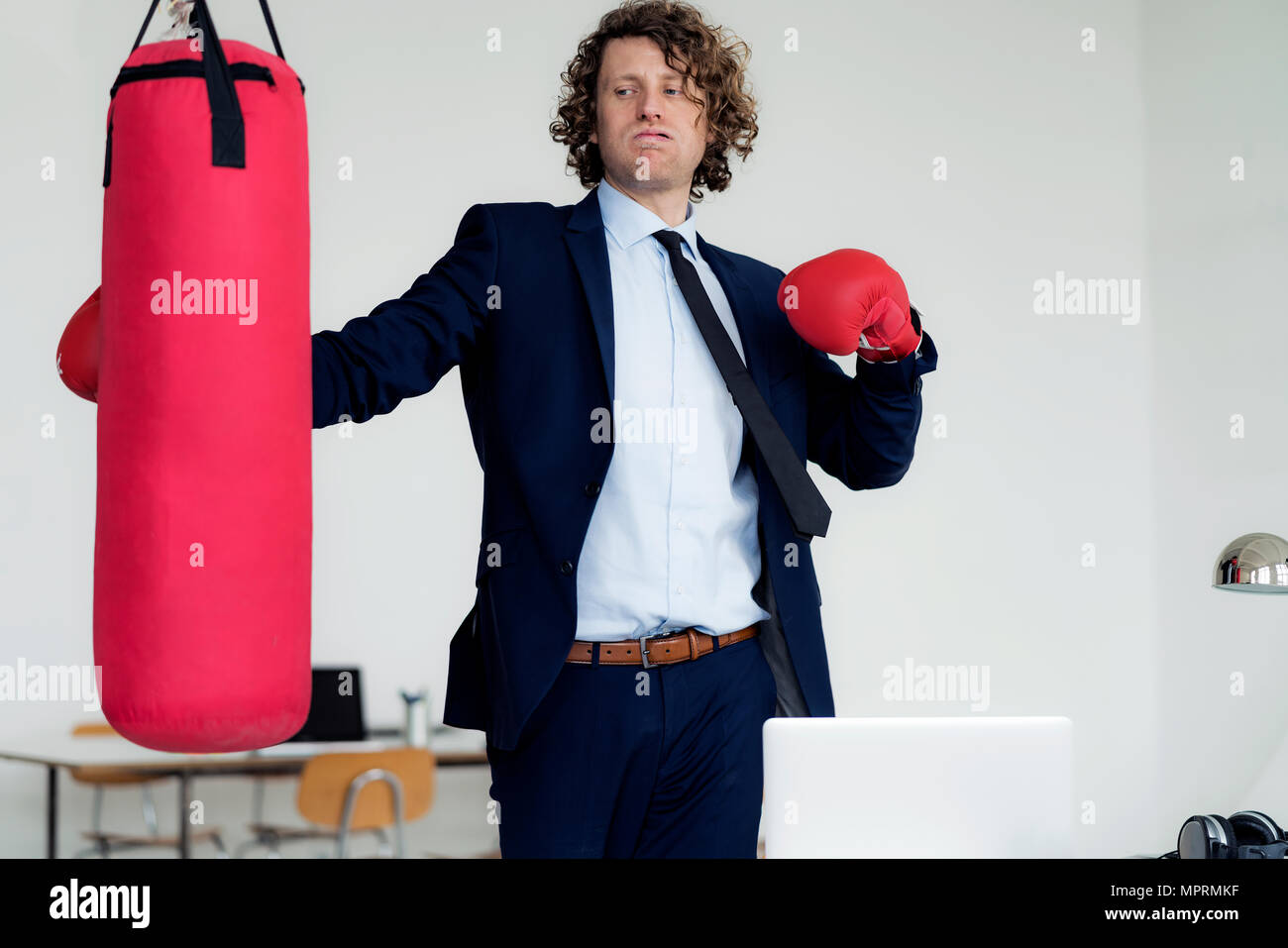 Stressed businessman frapper sac avec des gants de boxe dans son bureau Banque D'Images Stressed businessman frapper sac avec des gants de boxe dans son bureau Banque D'Images