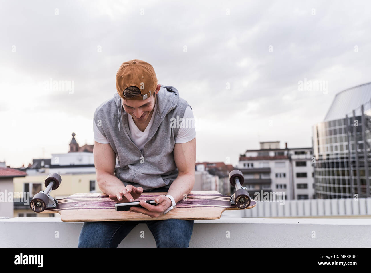 Smiling man sitting dans la ville avec skateboard using cell phone Banque D'Images