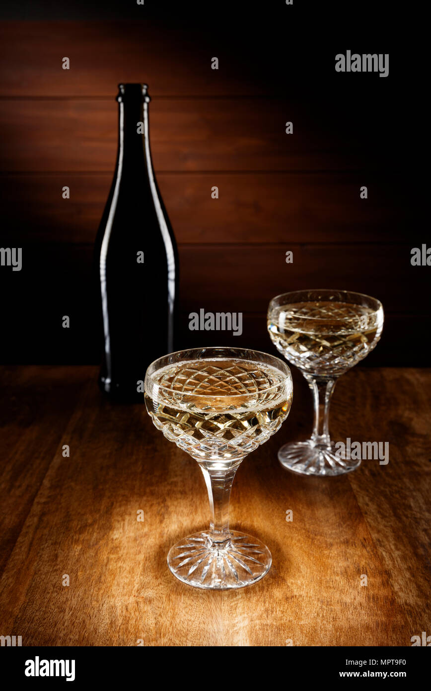 Plein feux sur les deux verres en cristal Champagne avec une bouteille en arrière-plan, tourné sur une table en bois ancien. Banque D'Images