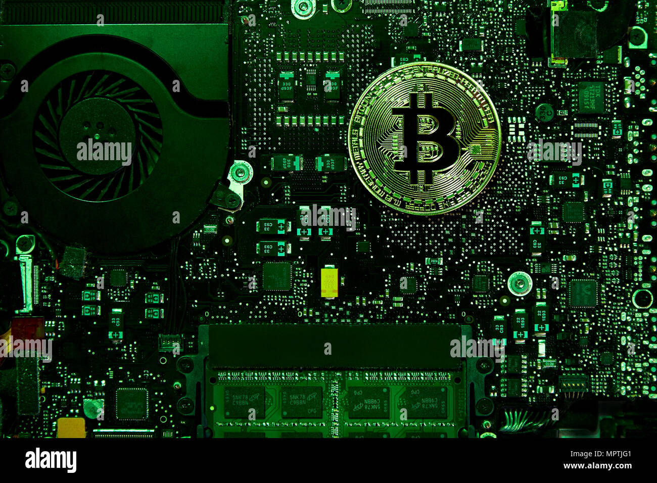 Une pièce physique Bitcoin assis sur une carte mère avec un ventilateur et de la RAM. Feu vert couvre la scène. En utilisant le domaine public d'un logo. Banque D'Images