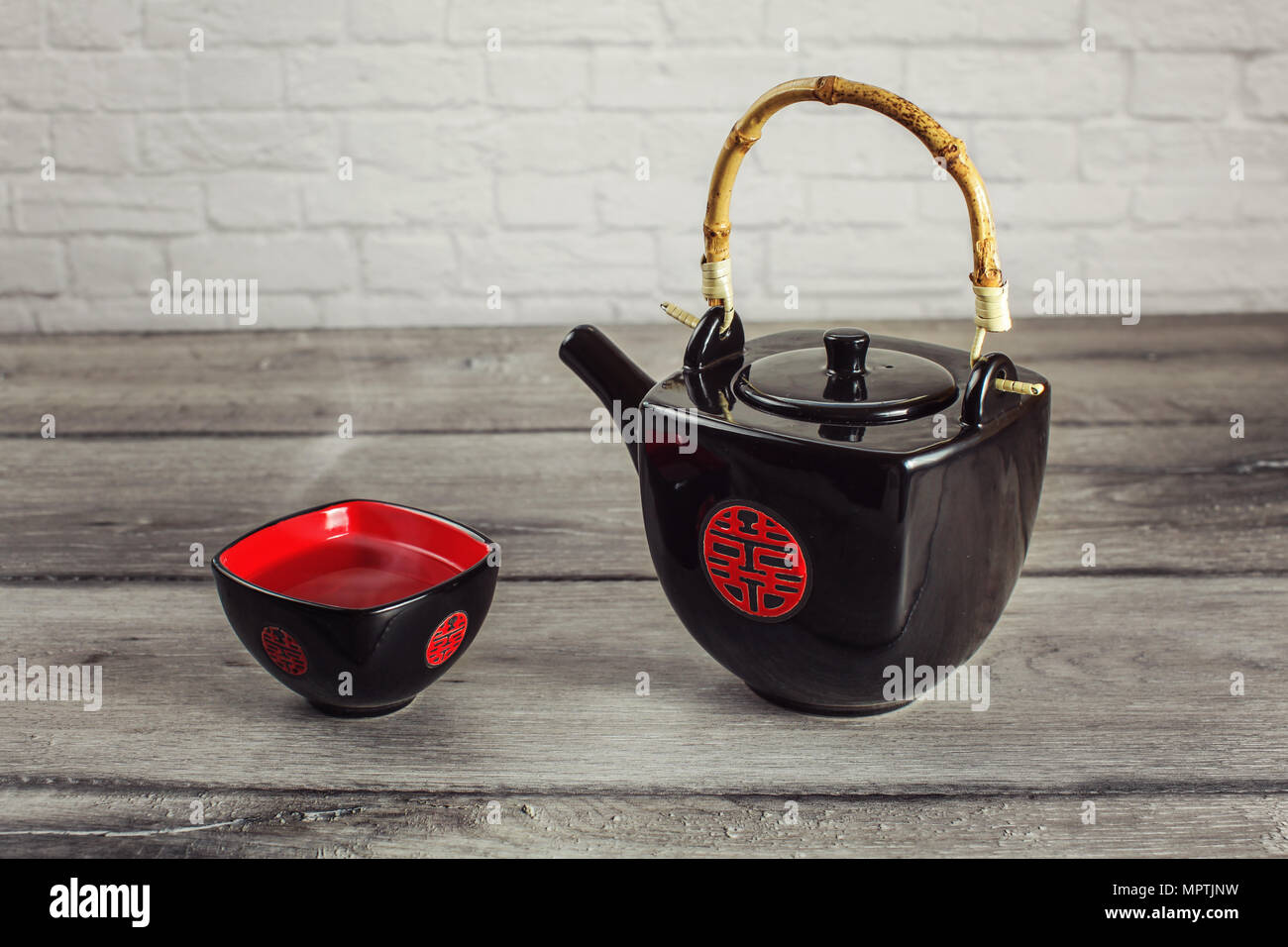 Carré noir théière et tasse pleine de thé chaud à la vapeur, avec sceau chinois rouge qui signifie "double bonheur", placé sur la table en bois gris. Banque D'Images