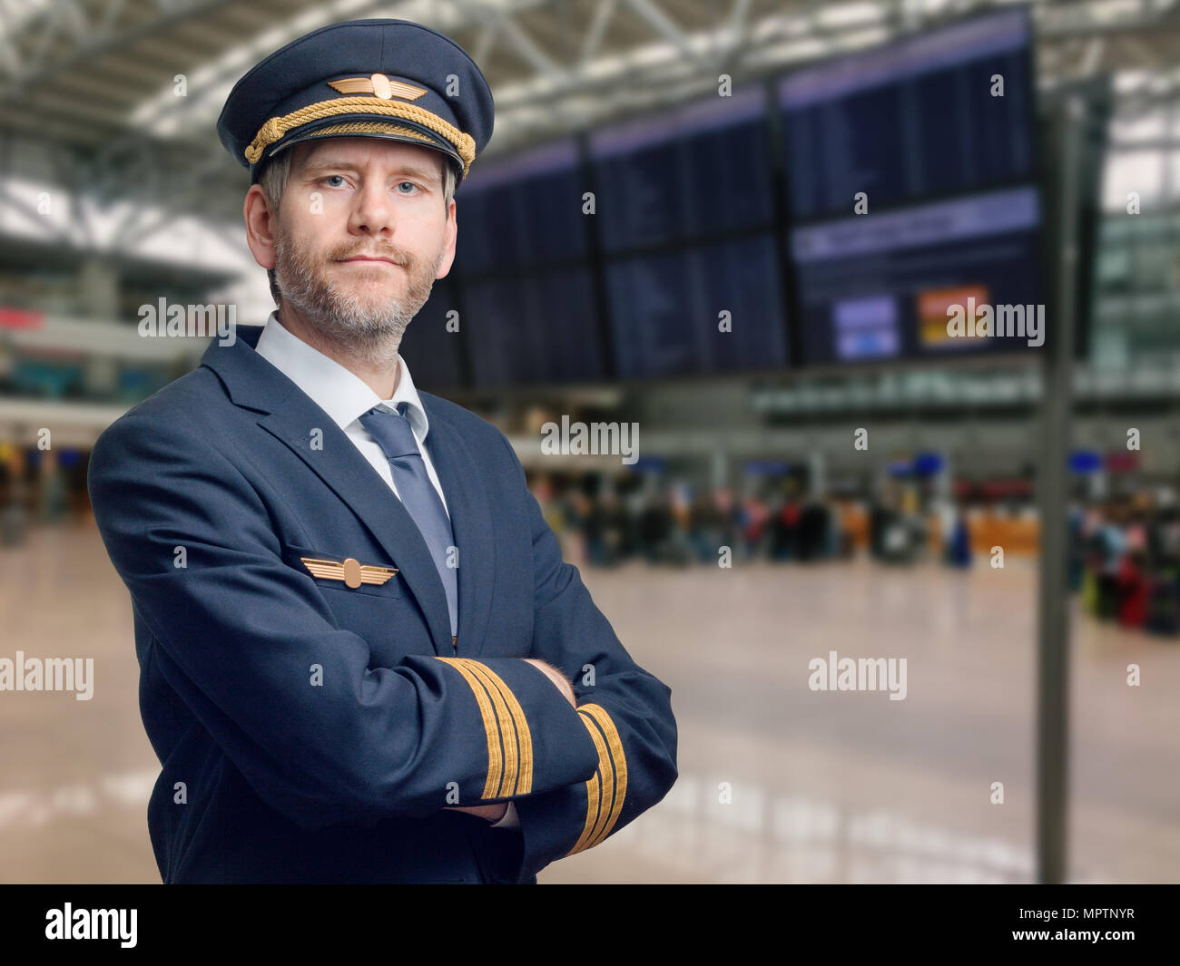 Portrait d'un pilote en uniforme avec des rayures d'or et cap croisa les bras. Il est debout dans le terminal d'un aéroport Banque D'Images