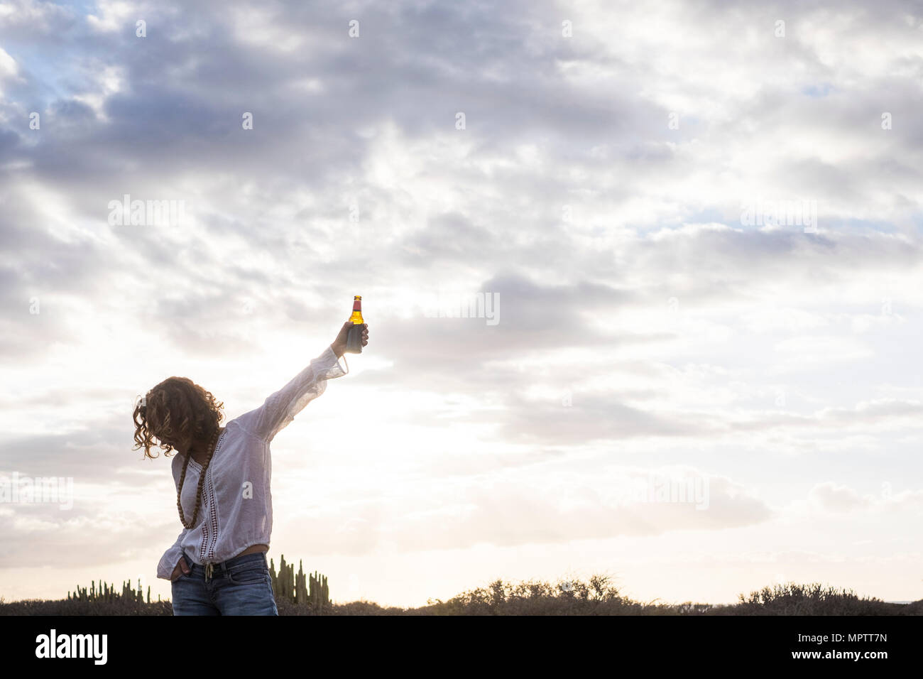 Beau et mignon 40 ans vieux modèle femelle avec de la bière à la main. rock'n roll poser pour la réussite et l'humeur. concept gagnant désert et nuages ciel dans le dos Banque D'Images