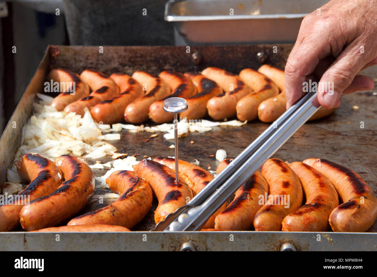 Côté masculins plus âgés avec des pinces saucisse tournant des hot dogs, des oignons sur un gril, cuisson au vendeur de rue. Vendeur de rue populaire américain cuisi Banque D'Images