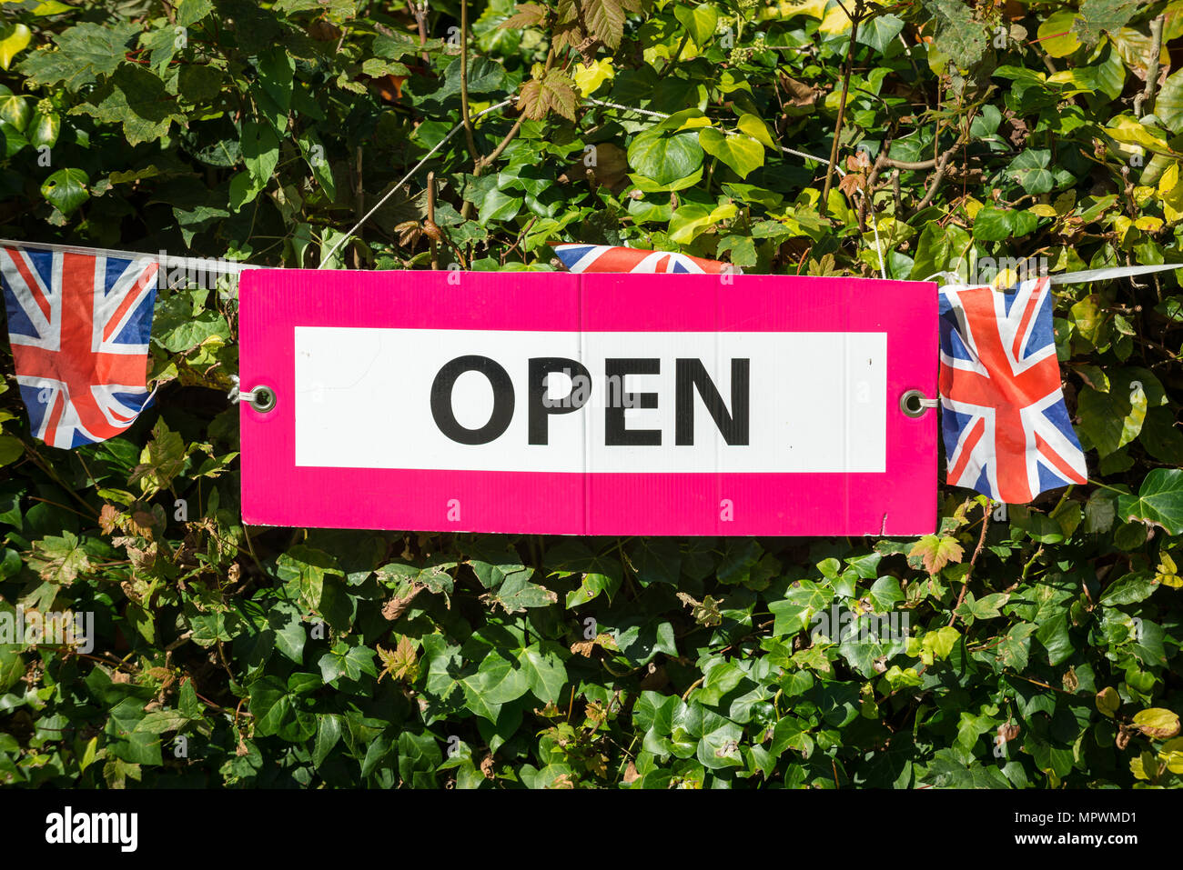 Union jack noir et d'un open sign hanging sur une haie. Banque D'Images