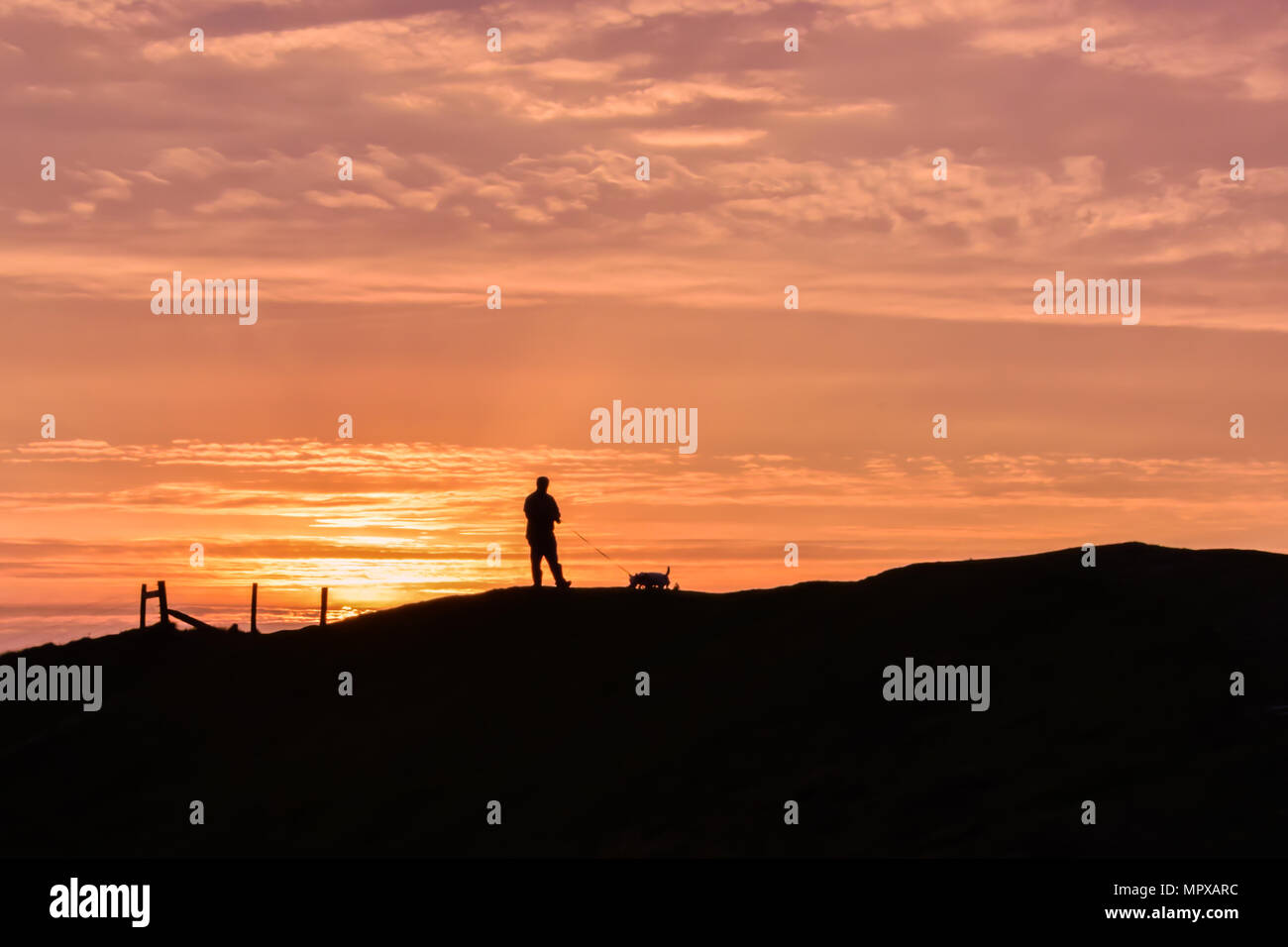 Silhouette de l'homme et le chien à marcher le long de la falaise à Dinas Dinlle magnifique coucher de soleil plage, Nord du Pays de Galles, Royaume-Uni Banque D'Images