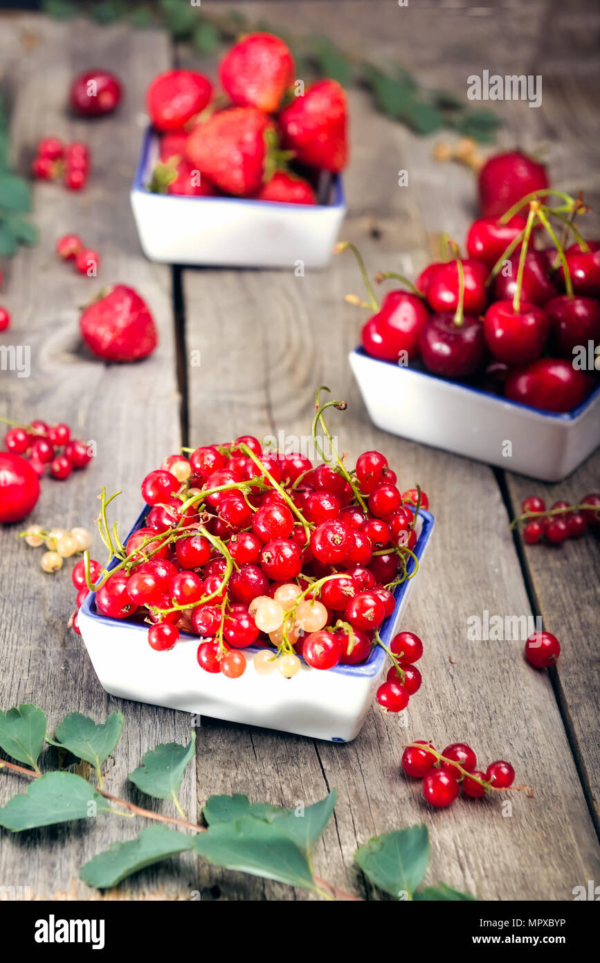 L'été frais Fruits rouges - fraise, cerise rouge et dans les bols de céramique sur la table en bois rustique. Régime alimentaire sain d'été. Concept de la récolte des agriculteurs. Focus sélectif, de l'espace pour le texte. Banque D'Images