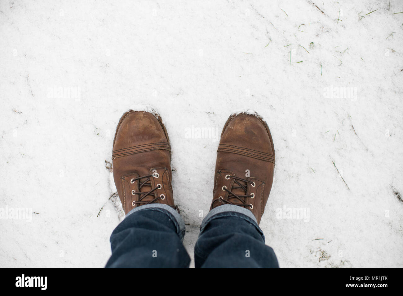 Pieds d'un homme portant des bottes de travail de l'aile rouge et bleu jeans debout dans la neige. Banque D'Images