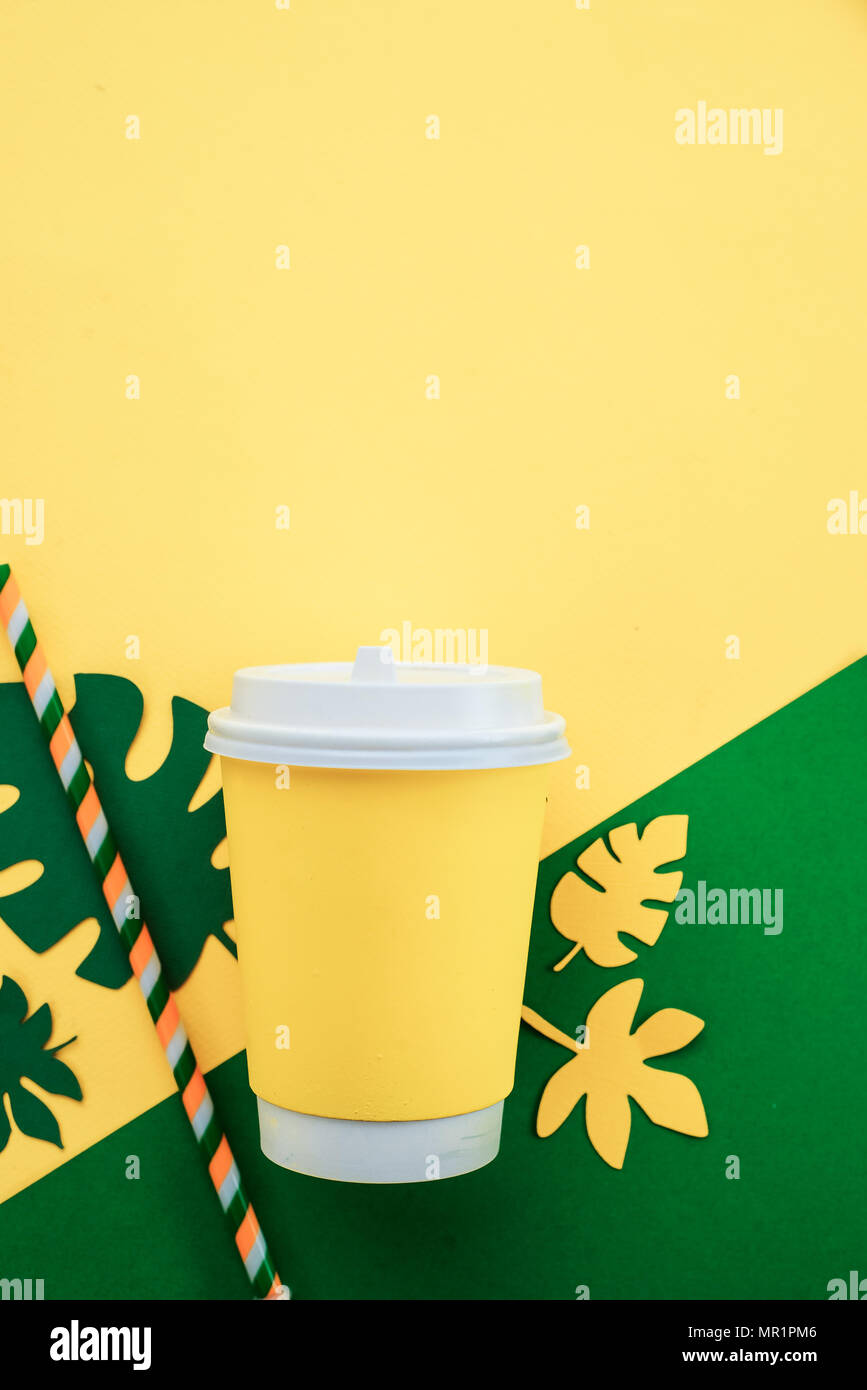 Tasse de papier avec une paille sur un fond jaune lumineux avec des feuilles tropicales, boisson d'été à rendez-vous avec concept copy space Banque D'Images