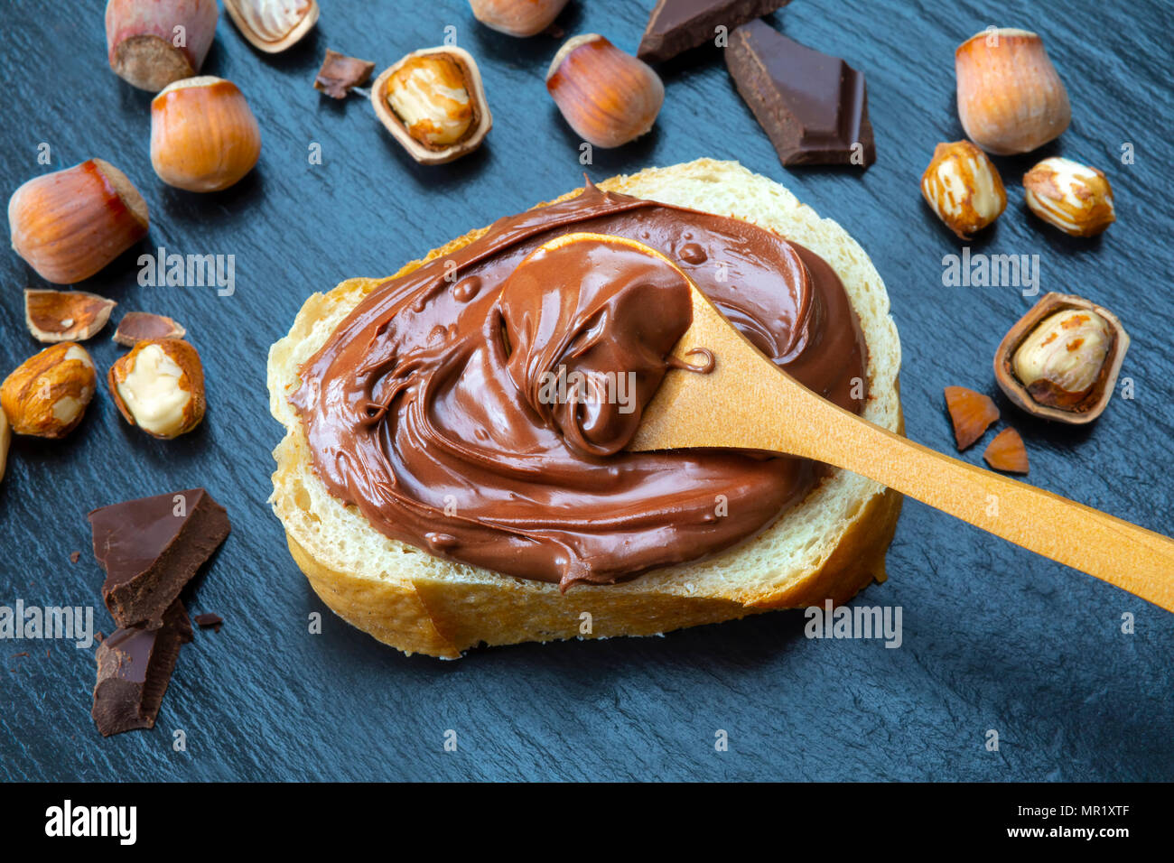 Tranche de pain avec la crème au chocolat et noisettes propagation sur le tableau noir. Servant un délicieux petit-déjeuner gratuit. Banque D'Images