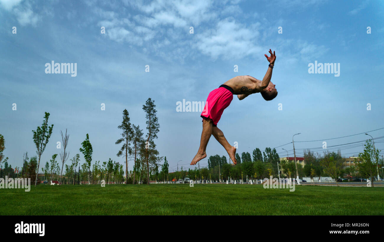 Tricking sur pelouse au parc. L'homme ne saut périlleux arrière. Les arts martiaux et le Parkour. Entraînement de la rue. Banque D'Images