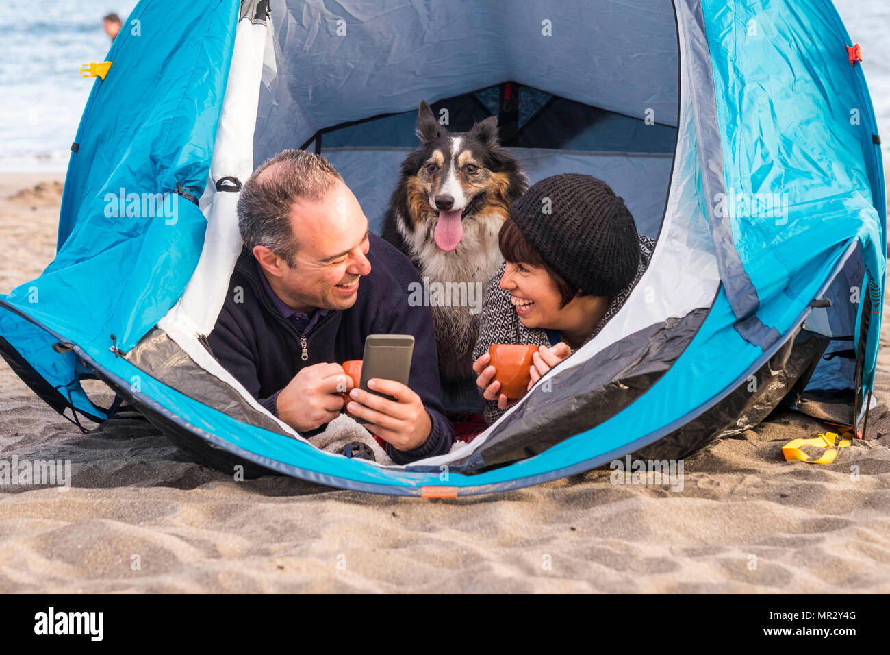 Belle belle paople avec chiot mignon à l'intérieur d'une tente à l'aide de téléphone portable pour envoyer un message ou prendre une photo. camping plage la liberté d'autres vacances j Banque D'Images