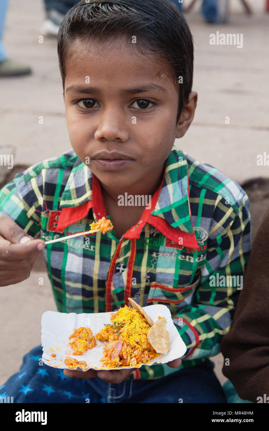 L'Inde, Uttar Pradesh, Varanasi, un garçon mange une collation de bhel puri sur les ghats. Banque D'Images