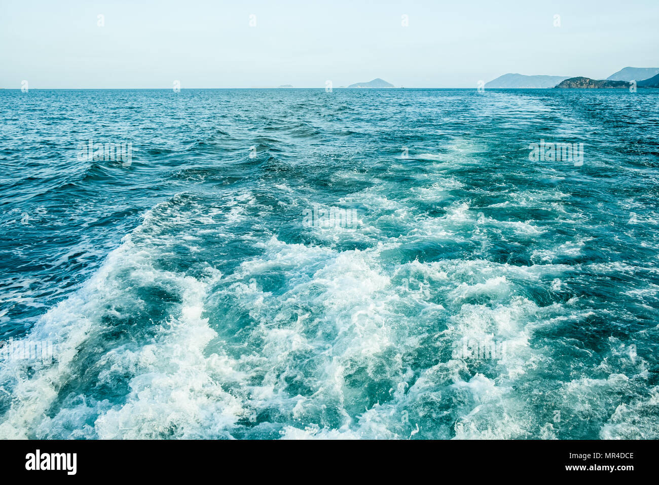 Tracé des courbes avec mousse blanche sur l'eau de mer de surface derrière fast moving bateau ou yacht. Les petites îles dans la brume sèche sur l'horizon. Ciel bleu avant le coucher du soleil. Banque D'Images