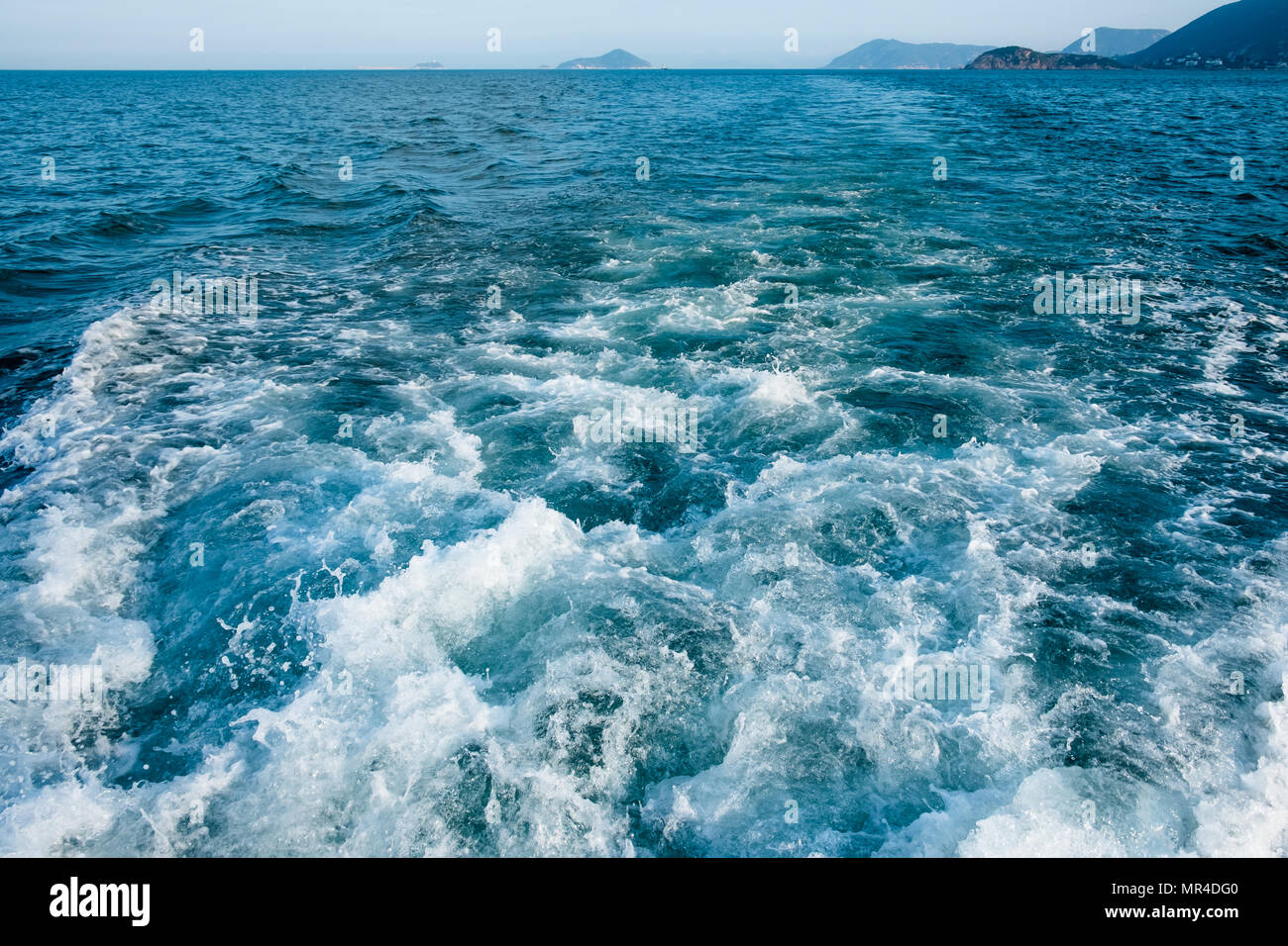 Tracé des courbes avec mousse blanche sur l'eau de mer de surface derrière fast moving bateau ou yacht. Les petites îles dans la brume sèche sur l'horizon. Ciel bleu avant le coucher du soleil. Banque D'Images