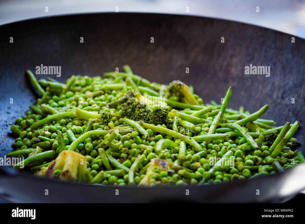 Close up sur les haricots verts, les brocolis et les petits pois sont cuits dans une grande poêle de fer. Banque D'Images