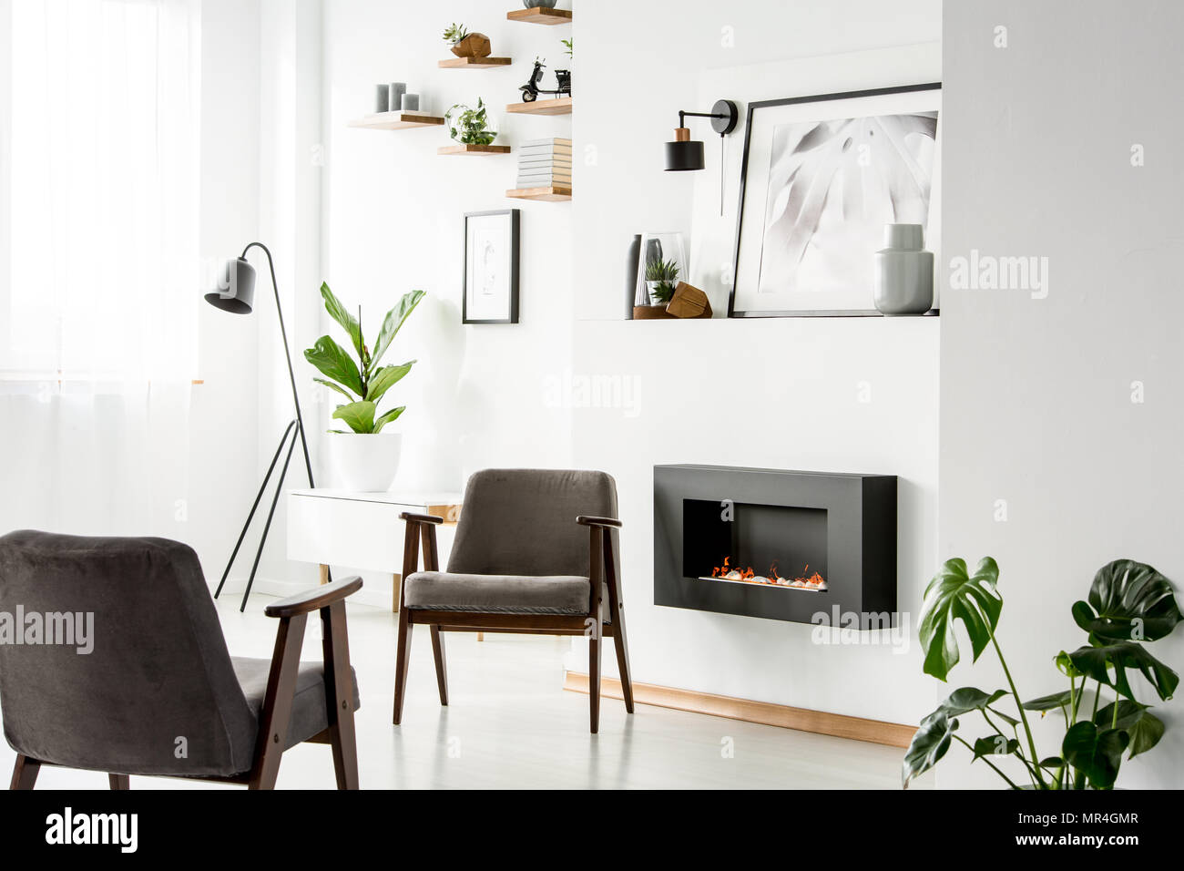 Fauteuils gris à côté de cheminée dans appartement blanc intérieur avec des plantes, et l'affiche de la lampe. Photo réelle Banque D'Images