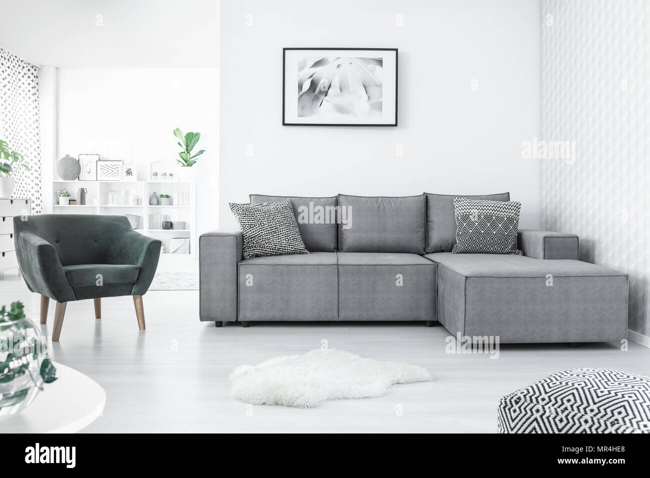 Fauteuil gris et canapé d'angle, la peinture sur le mur blanc et pouf dans un salon moderne intérieur Banque D'Images