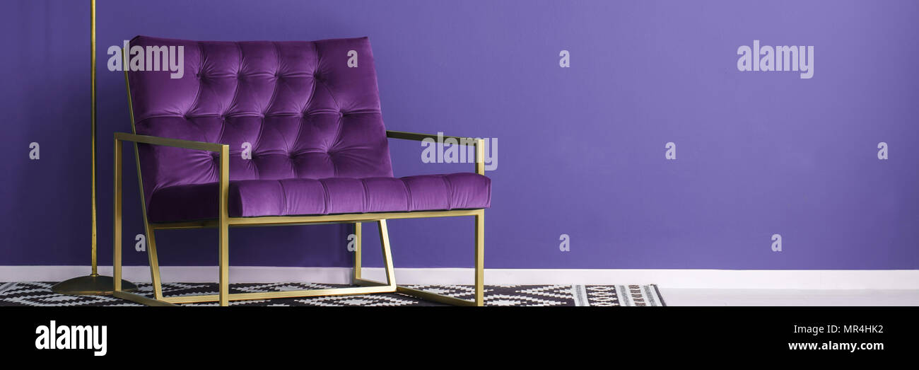 Fauteuil violet avec cadre métallique d'or debout sur un tapis noir et blanc à motifs violet à l'intérieur de la salle de lecture. Placez votre produit ici Banque D'Images