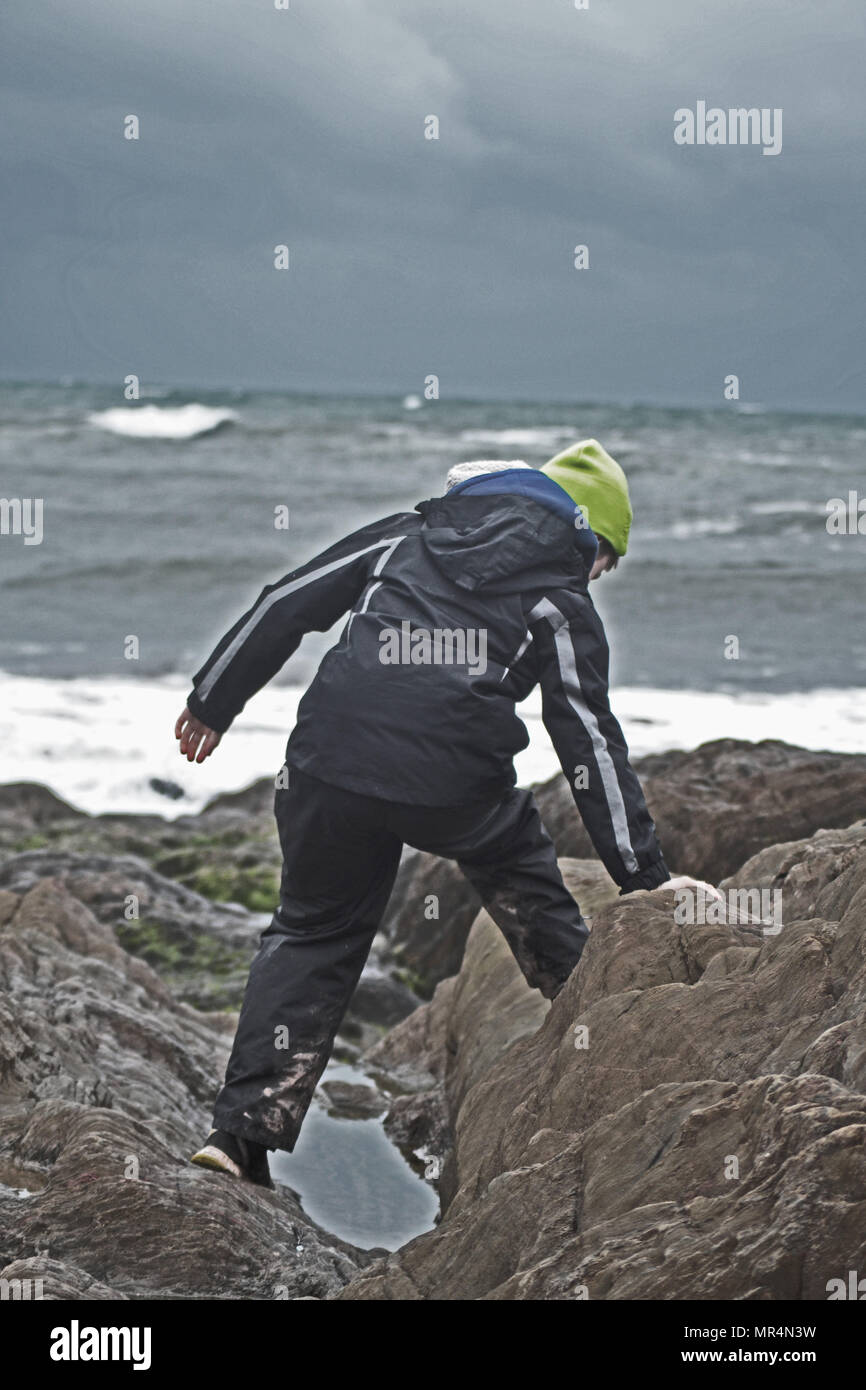 Garçon escalade dans les rochers au bord de la mer, sur un jour moody Banque D'Images