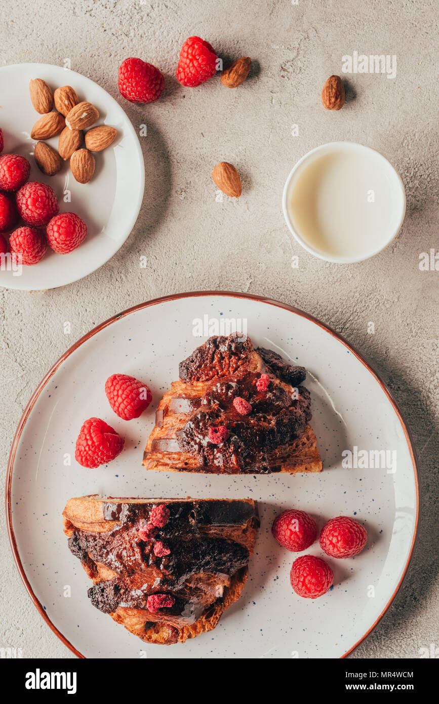 Mise à plat avec 1 tasse de lait, des pâtisseries, de framboises et d'amandes sur les plaques sur la table lumineuse Banque D'Images