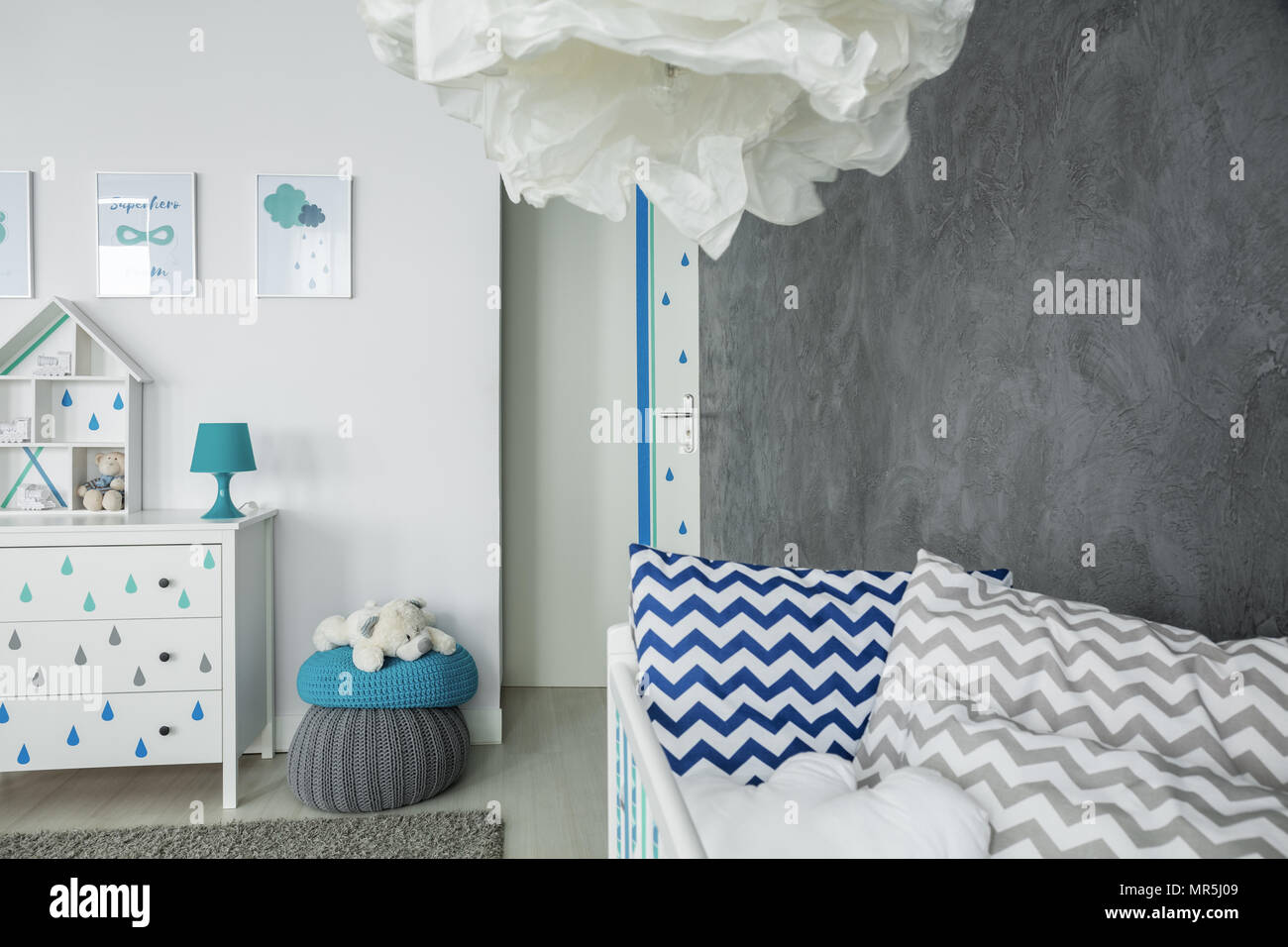 Chambre enfant avec mur de béton, lit bébé et commode blanche Banque D'Images