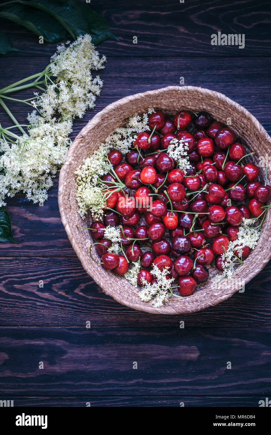 Cerises fraîches et de fleurs dans un panier sur la table rustique en bois Banque D'Images