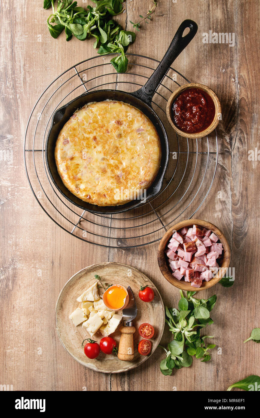 Omelette Espagnole tortilla avec bacon servi en fonte pan avec la sauce et les ingrédients ci-dessus sur fond de bois. Vue de dessus, de l'espace. Banque D'Images