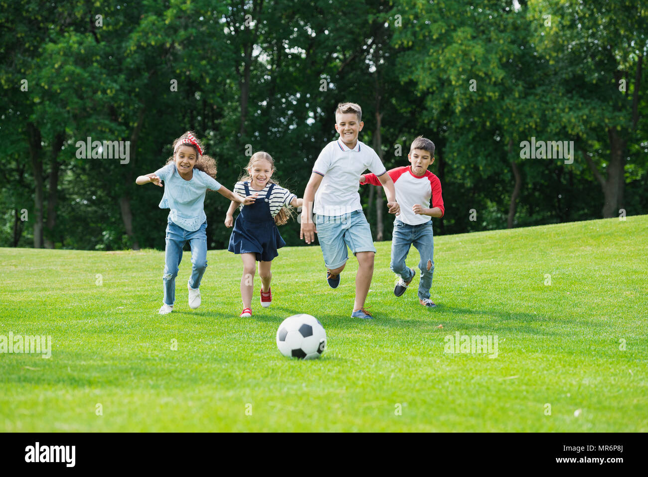 Happy Cute kids multiethnique à jouer au soccer avec ball in park Banque D'Images