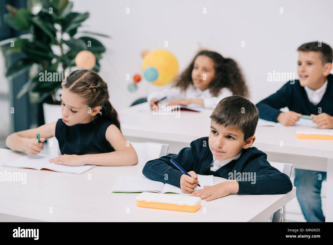 Mignon petit écoliers assis à un bureau et de l'écriture dans les livres d'exercice Banque D'Images