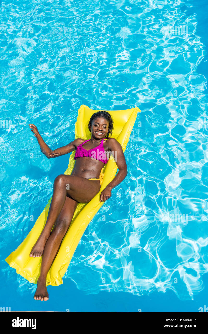 African American Woman flottant sur le matelas gonflable dans la piscine Banque D'Images