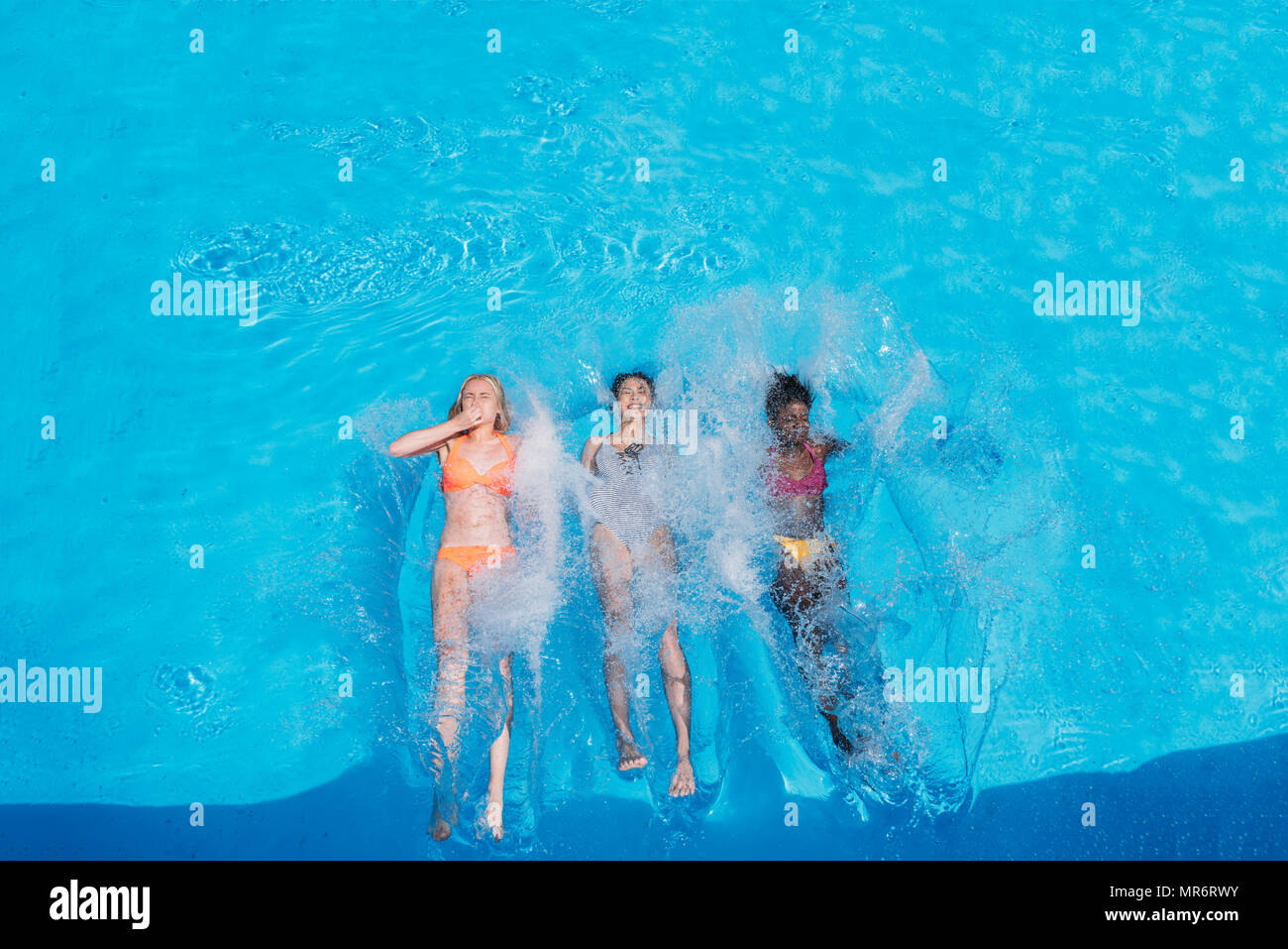 Trois femmes multiethniques heureux natation sur le dos dans la piscine de resort Banque D'Images