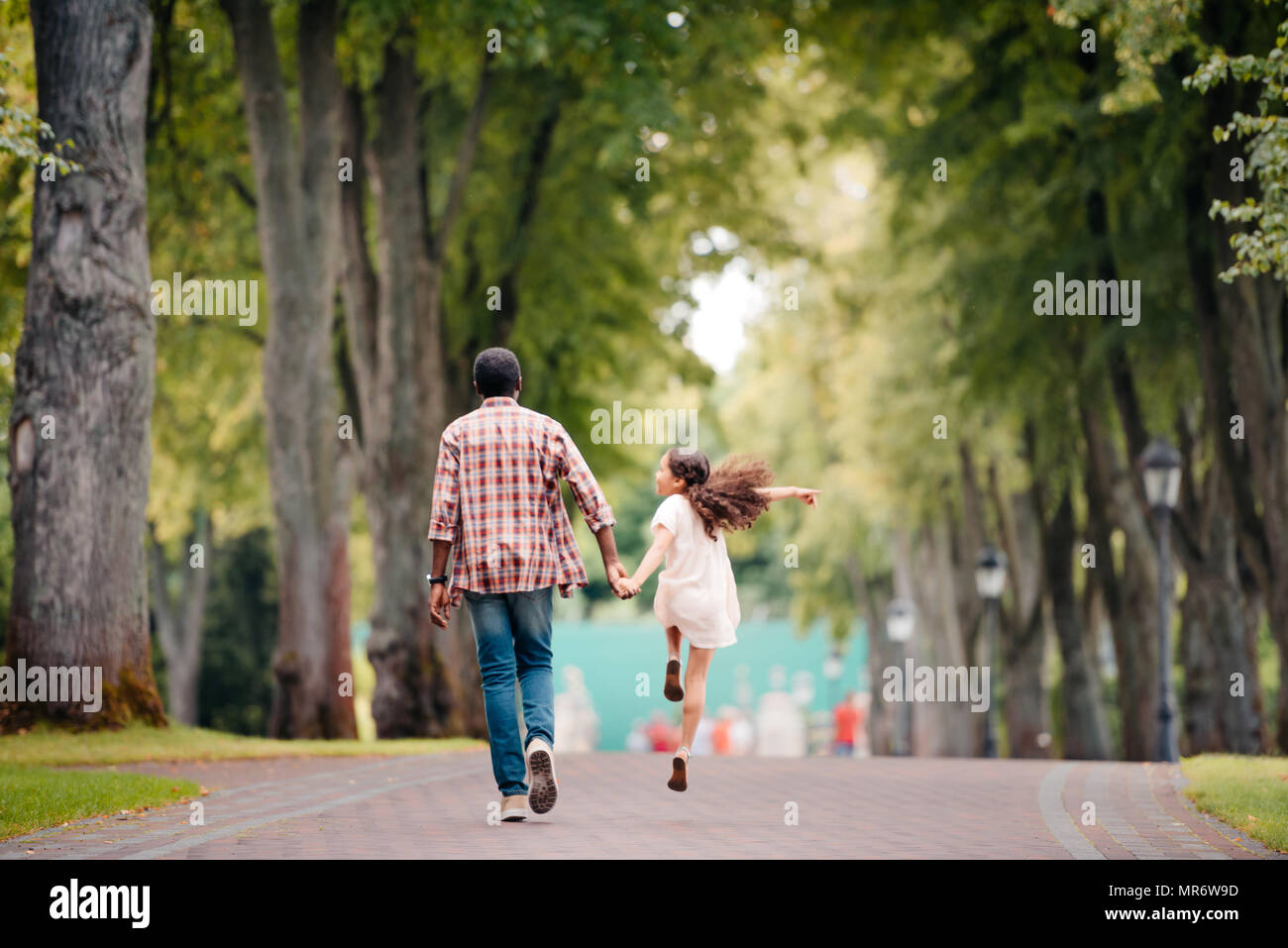 Vue arrière de l'african american girl holding hands avec grand-père, le saut et walking in park Banque D'Images