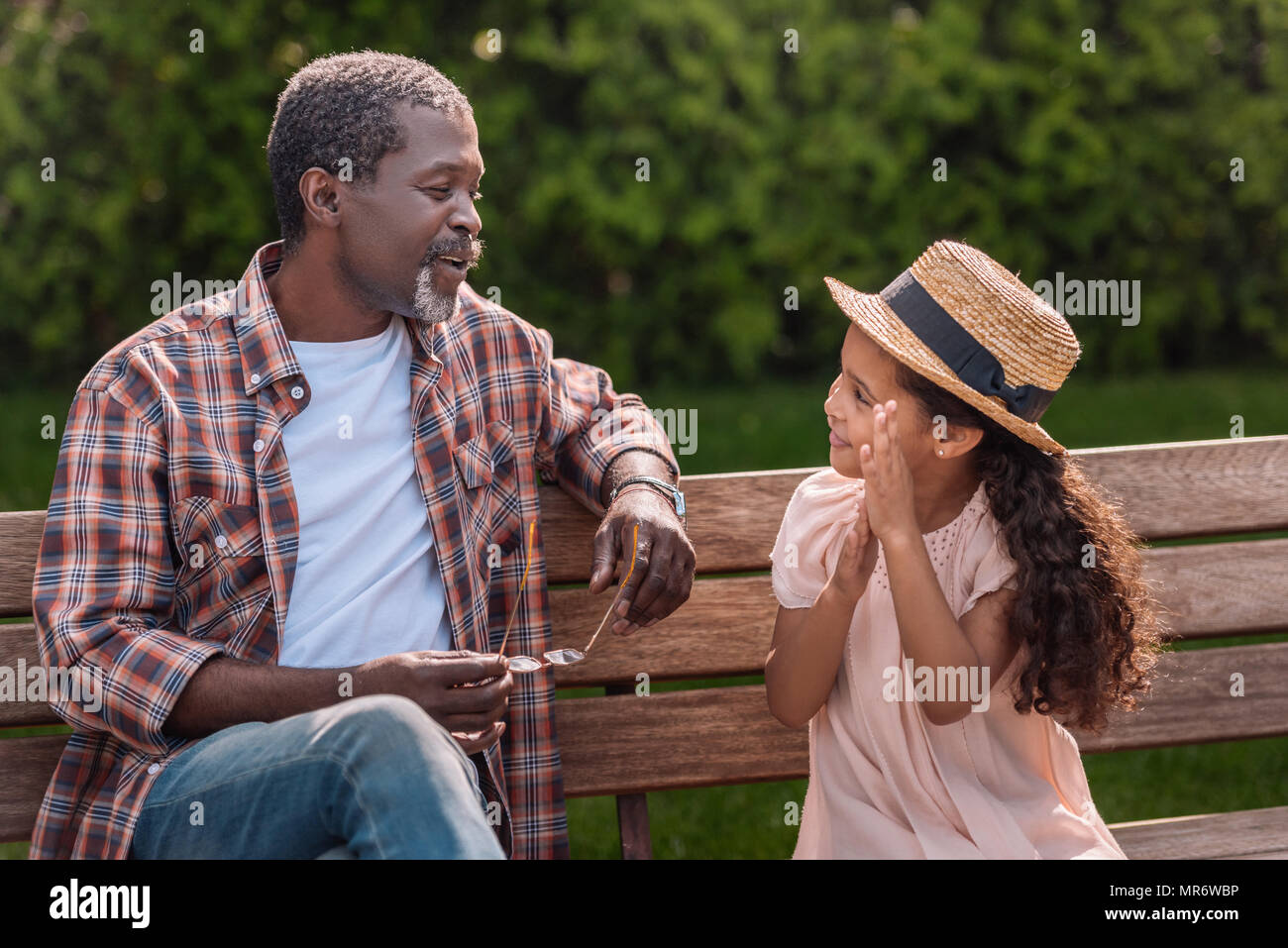 Adorable petite fille afro-américaine de parler avec son grand-père assis sur un banc dans le parc Banque D'Images