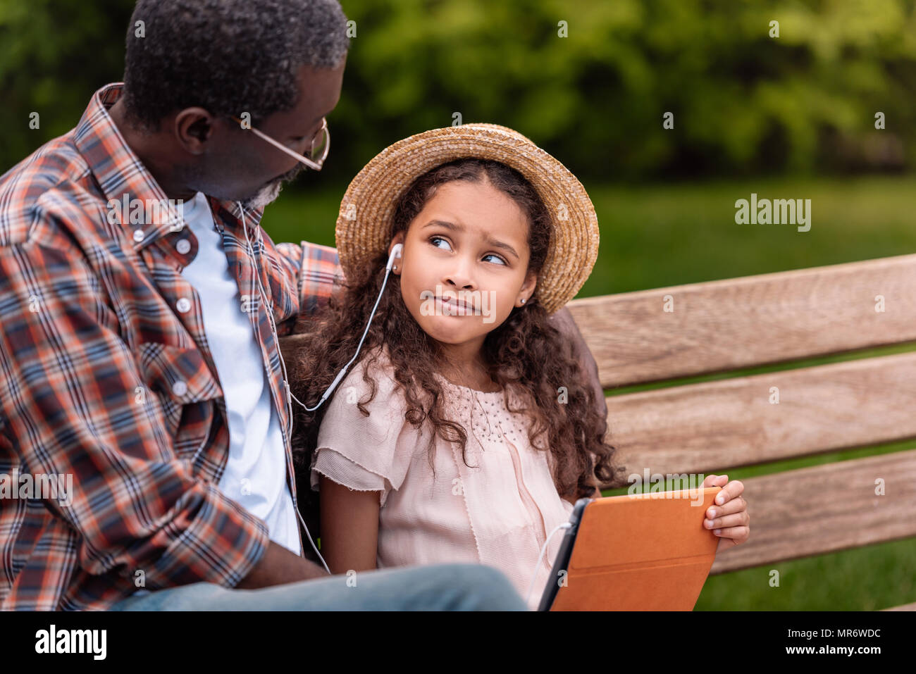 African American petit-fils et son grand-père à l'écoute de la musique sur digital tablet while sitting on bench in park Banque D'Images