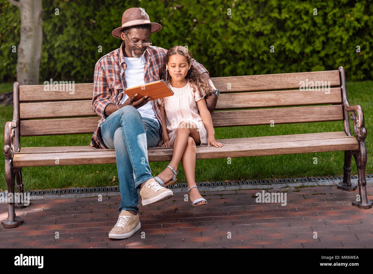 African American petit-fils et son grand-père à l'écoute de la musique sur digital tablet while sitting on bench in park Banque D'Images