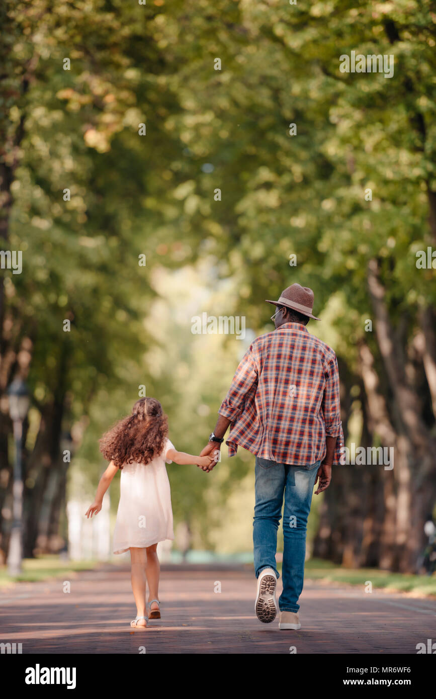 Vue arrière de l'african american girl holding hands avec grand-père et de la marche dans l'Allée Verte Banque D'Images