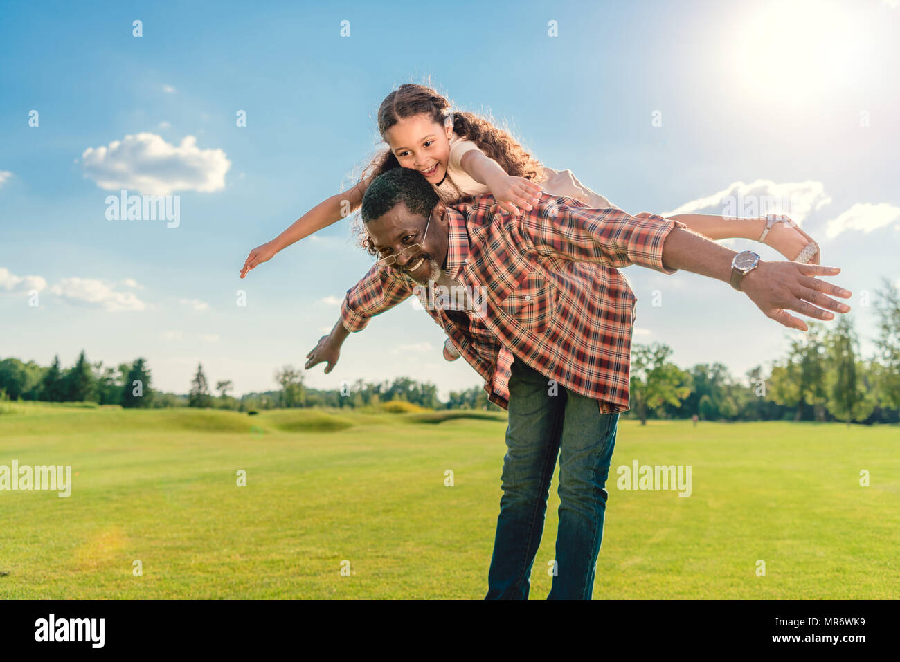 African American grand-père-fille donner piggyback ride sur pelouse verte et de la lumière du soleil Banque D'Images