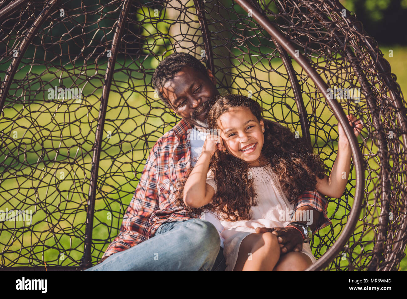 Happy african american petite-fille et grand-père de passer du temps ensemble à se balancer fauteuil suspendu dans park Banque D'Images