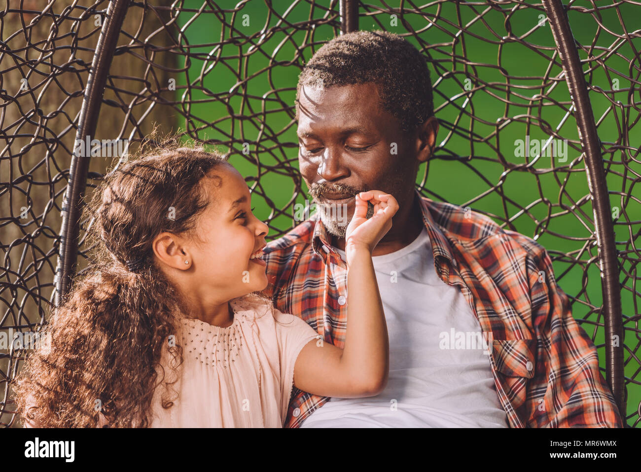 Happy african american petite-fille et son grand-père assis en balançant fauteuil suspendu dans park Banque D'Images